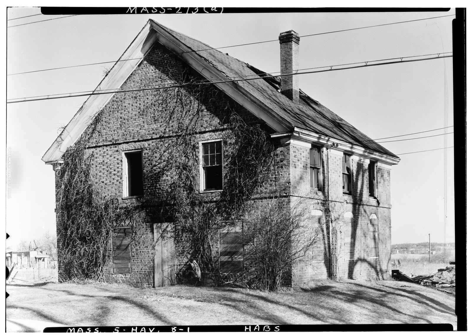 Black-and-white Historic American Buildings Survey photograph of the Duston Garrison House in Haverhill: a two-story brick house with a chimney, some windows boarded, vines on the wall.
